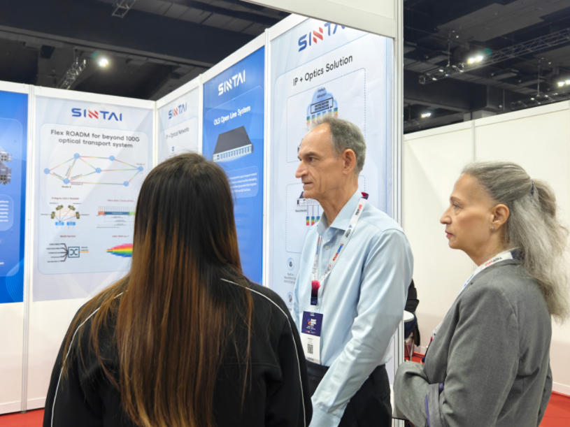 Two event attendees listening as a Sintai staff member speaks to them in front of the company's booth. Two event attendees listening as a Sintai staff member speaks to them in front of the company's booth.